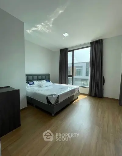 Spacious bedroom with large window and modern furnishings in a bright apartment.