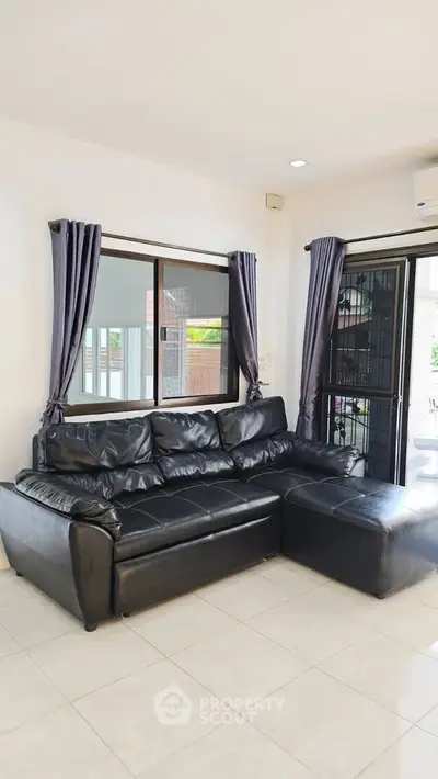 Spacious living room with black leather sectional sofa and large windows for natural light.