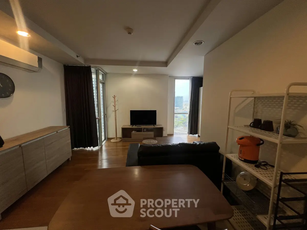 Modern living room with wooden flooring, cozy seating, and a TV, featuring a balcony with city views.