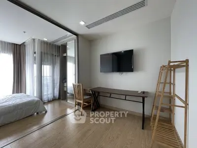 Modern bedroom with wooden flooring, wall-mounted TV, and sliding glass doors leading to a cozy bed area.
