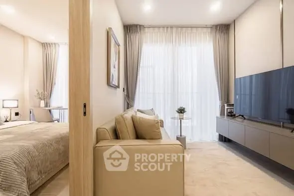 Modern living room with sleek TV unit and cozy beige sofa, adjacent to a stylish bedroom with elegant decor.