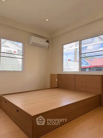 Spacious bedroom with modern wooden platform bed and large windows for natural light.