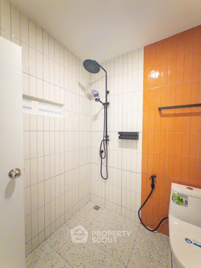 Modern bathroom with sleek shower and vibrant orange accent wall