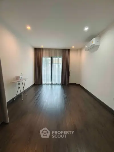 Spacious empty room with wooden flooring and large window, perfect for customization.
