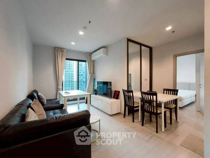 Modern living room with dining area and city view, featuring sleek furniture and natural light.