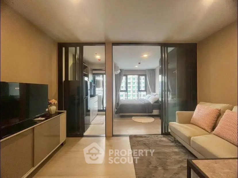 Modern living room with glass doors leading to a cozy bedroom, featuring stylish furniture and a TV unit.