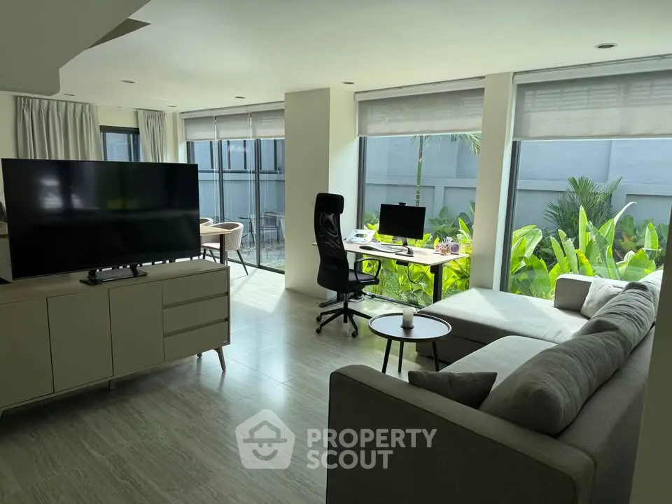 Modern living room with large windows and garden view, featuring sleek furniture and natural light.