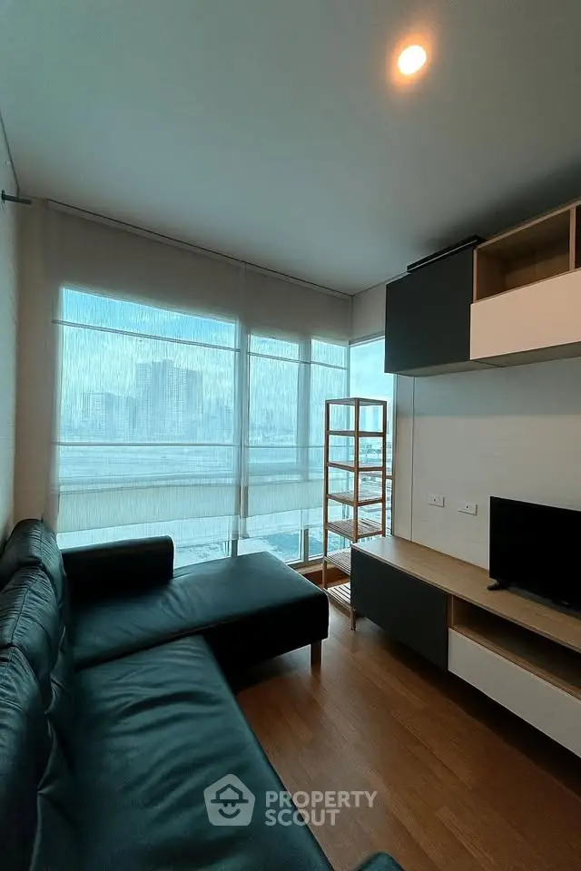 Modern living room with sleek black sofa and city view through large windows.
