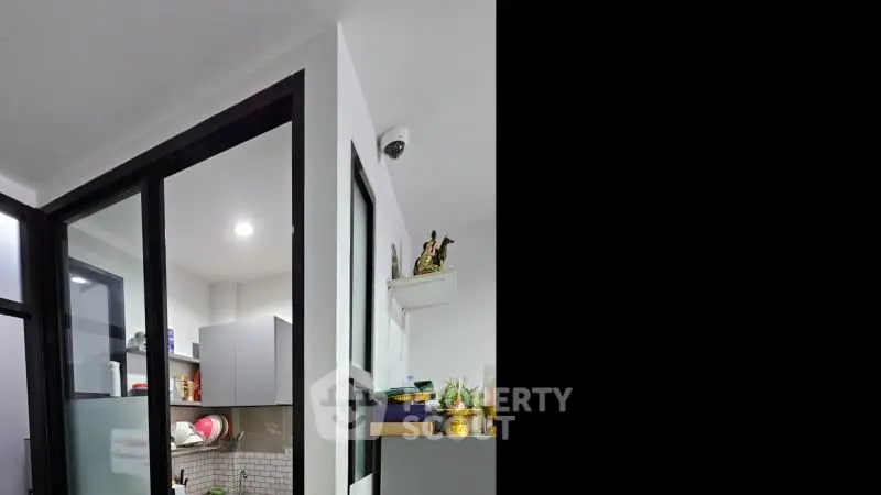 Modern kitchen with sleek cabinets and open layout, featuring a security camera and decorative shelf.