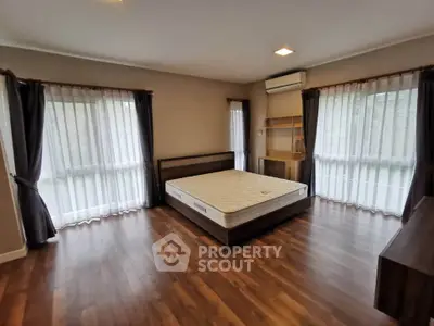 Spacious bedroom with large windows and wooden flooring, featuring a bed and air conditioning.
