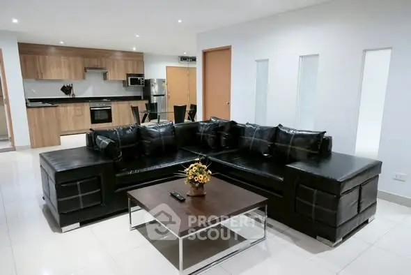 Modern living room with sleek black leather sectional and stylish kitchen in open layout