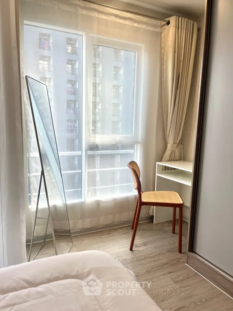 Bright bedroom with large window, stylish chair, and full-length mirror