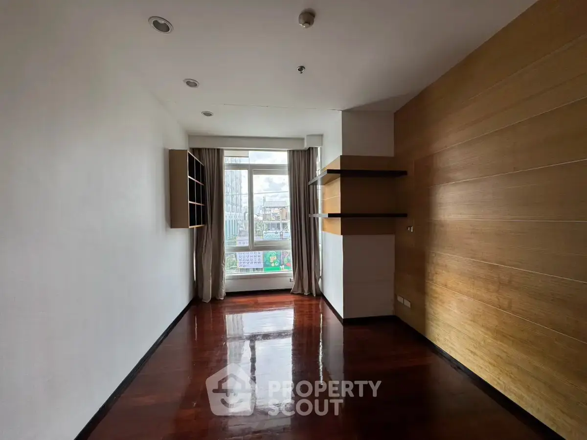 Spacious room with wooden flooring and large window offering city views.