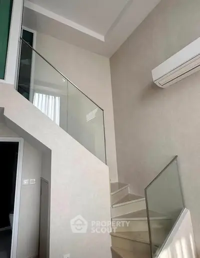 Modern staircase with glass railing and air conditioning in a bright interior space.