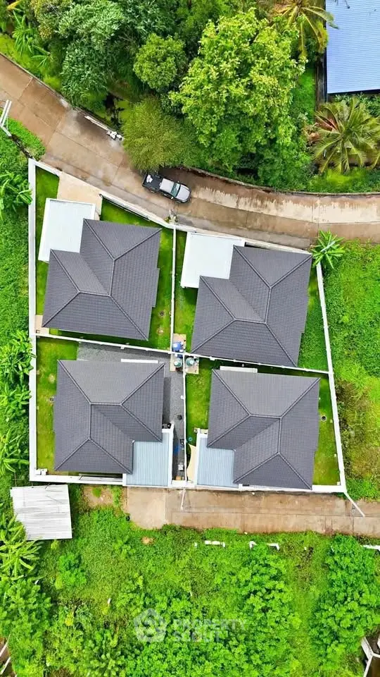 Aerial view of modern residential complex with lush greenery and paved pathways.
