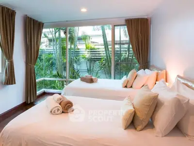 Spacious bedroom with large windows and garden view, featuring two neatly made beds and elegant decor.