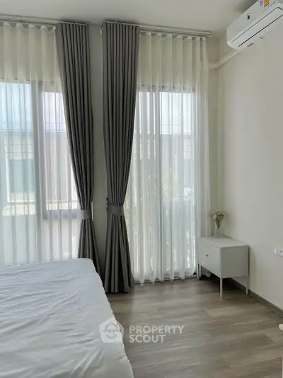 Bright bedroom with large windows and elegant curtains, featuring a minimalist design and air conditioning.