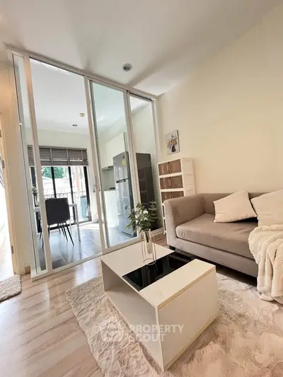 Modern living room with cozy sofa and sleek coffee table, open layout to kitchen with glass doors.