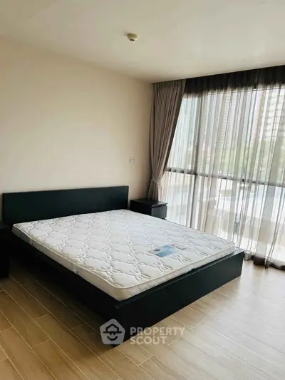 Spacious bedroom with large window and modern bed frame in a bright apartment.