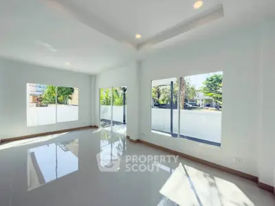Spacious sunlit living room with large windows and glossy tiled floors in modern home.