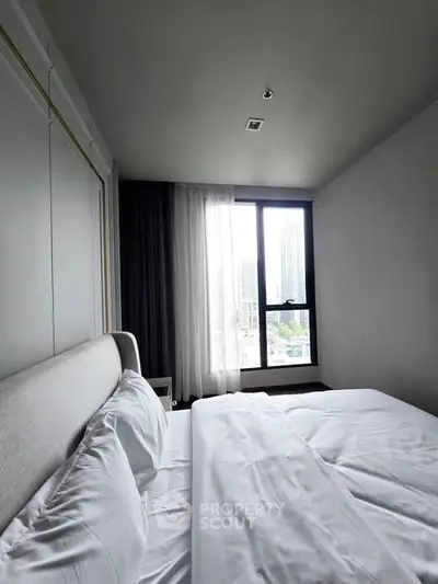 Modern bedroom with city view, featuring a comfortable bed and large window.