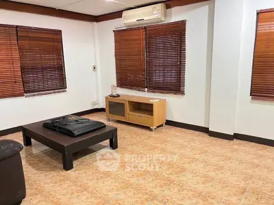 Spacious living room with air conditioning and wooden blinds, featuring tiled flooring and minimalist furniture.
