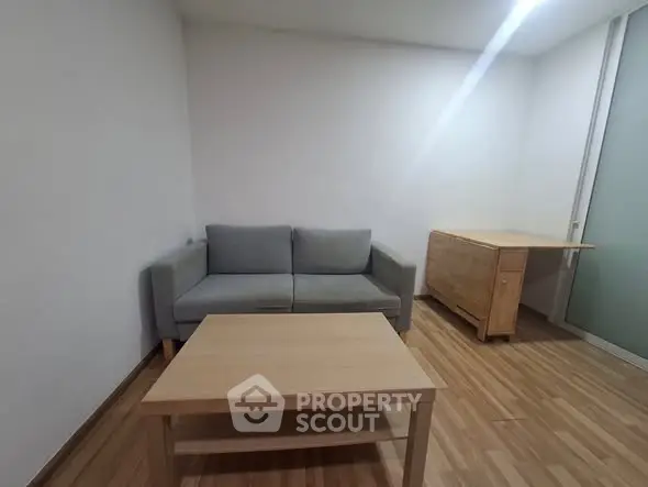 Minimalist living room with wooden flooring, gray sofa, and wooden furniture.