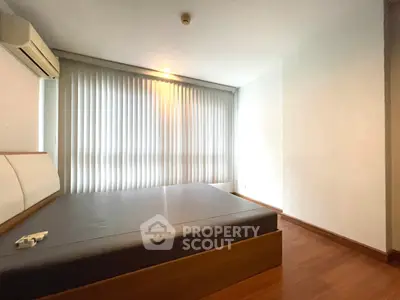 Spacious bedroom with wooden flooring and large window with blinds in modern apartment.