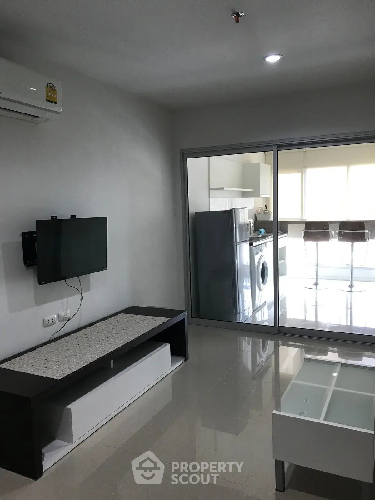 Modern living room with sleek furniture and glass partition leading to kitchen area.