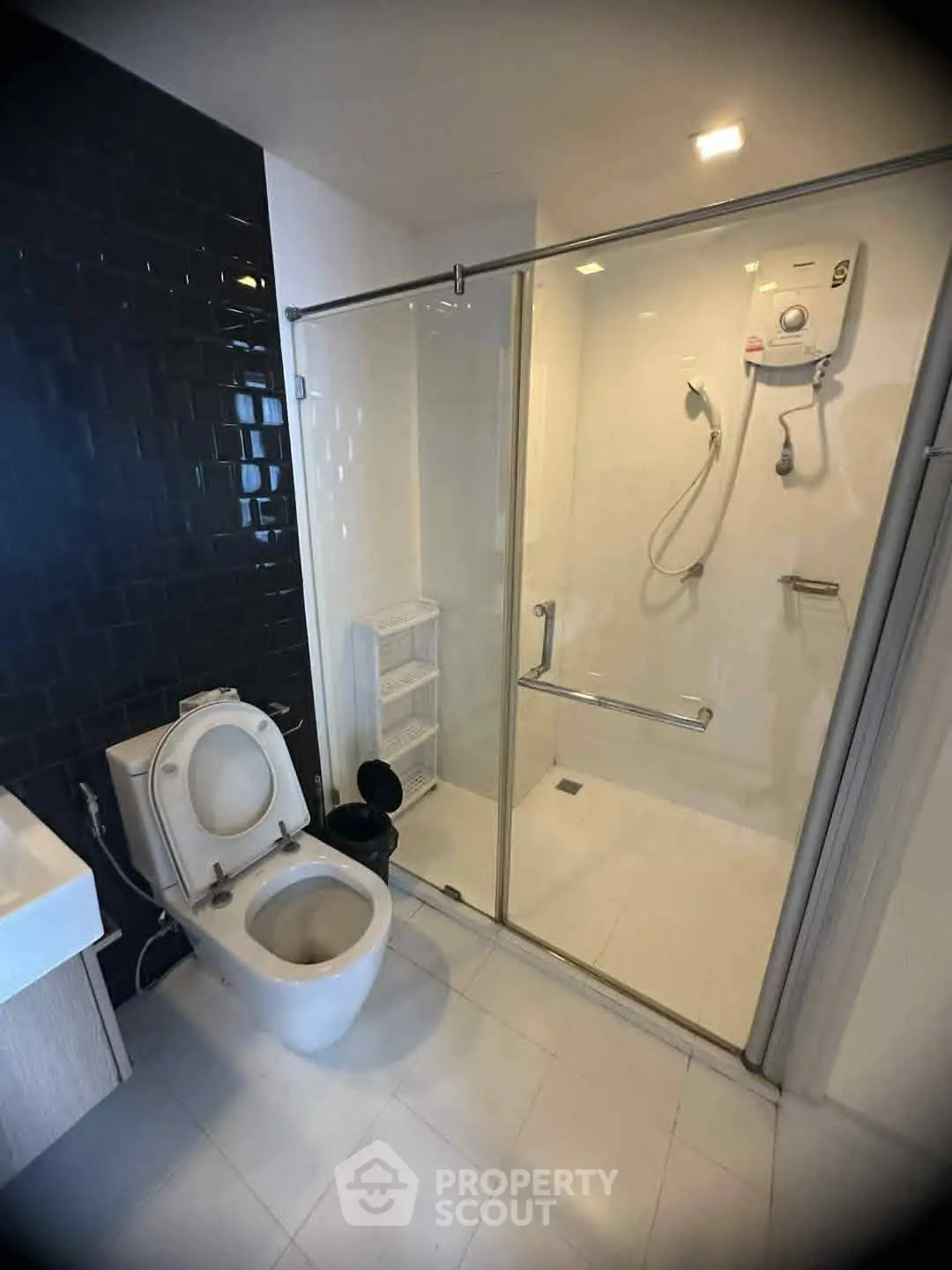 Modern bathroom with glass shower and sleek black tile accent wall.