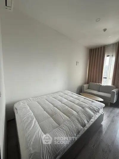 Modern bedroom with cozy bed and stylish sofa, featuring large window with city view.