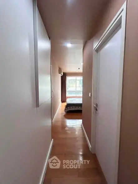 Bright hallway leading to a cozy bedroom with wooden flooring and natural light.