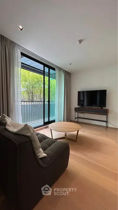 Modern living room with large window and balcony view, featuring stylish furniture and natural light.