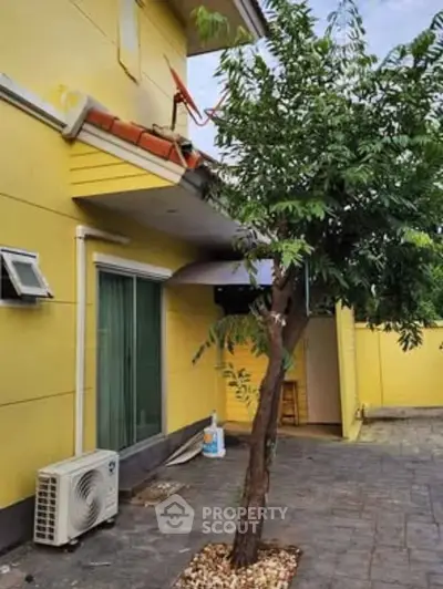 Charming yellow exterior with tree and patio, perfect for outdoor relaxation.