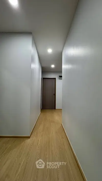 Modern minimalist hallway with wooden flooring and recessed lighting.