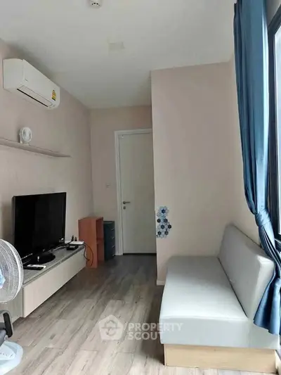 Modern living room with sleek furniture and large window, featuring a TV and air conditioning.