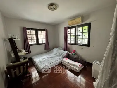 Cozy bedroom with wooden flooring, air conditioning, and natural light from two windows.