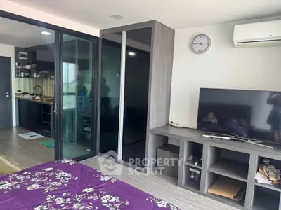 Modern bedroom with sleek furniture and open kitchen layout, featuring a wall-mounted TV and air conditioning.