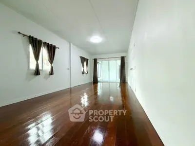 Spacious empty living room with polished wooden floors and large windows for natural light.