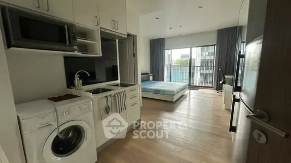 Modern studio apartment with open layout, featuring kitchen appliances and a bright living area with balcony view.