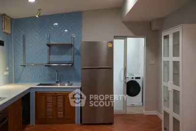 Modern kitchen with stainless steel fridge and washing machine, featuring blue herringbone backsplash and terracotta tiles.
