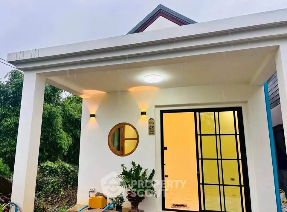 Charming modern house entrance with unique round window and stylish lighting, surrounded by lush greenery.
