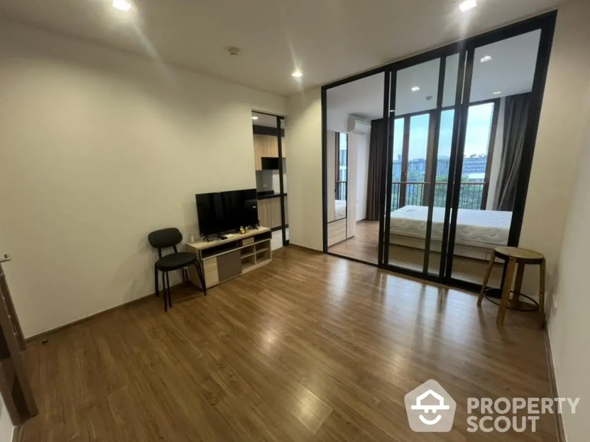 Spacious modern living room with wooden flooring and large glass doors leading to a cozy bedroom.