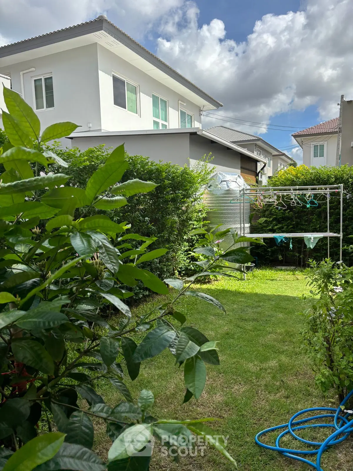 Charming suburban garden with lush greenery and modern house exterior under a bright blue sky.