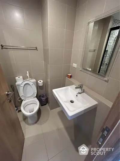 Modern bathroom with sleek fixtures and neutral tiles, featuring a wall-mounted sink and toilet.