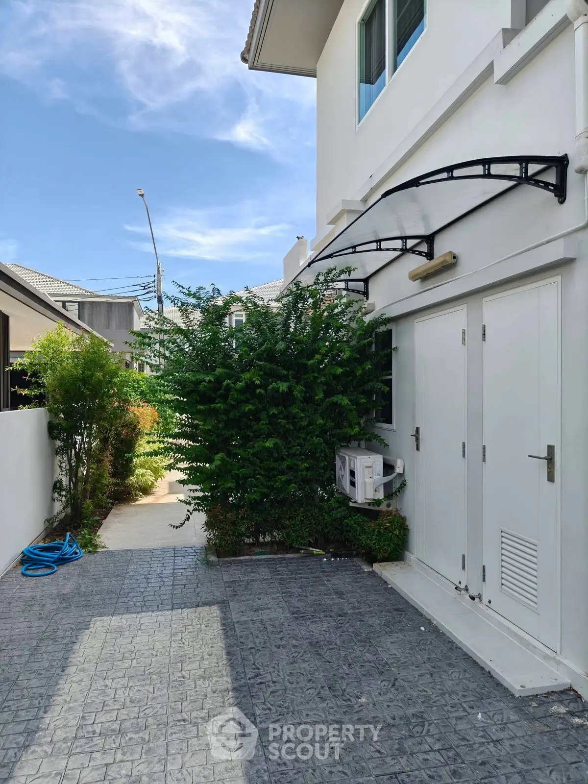 Modern house exterior with paved walkway and lush greenery, showcasing contemporary design and outdoor space.
