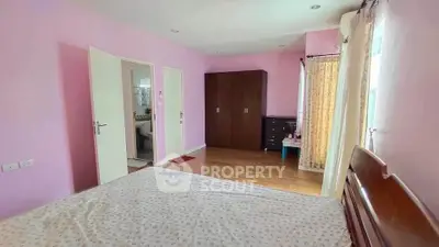 Spacious bedroom with wooden furniture and pink walls, featuring a large wardrobe and natural light.