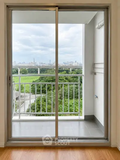 Modern apartment balcony with stunning city and greenery view through sliding glass doors.