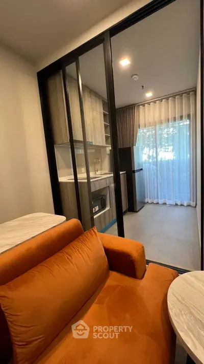 Modern open-layout living room with orange sofa and kitchen view, featuring floor-to-ceiling windows.