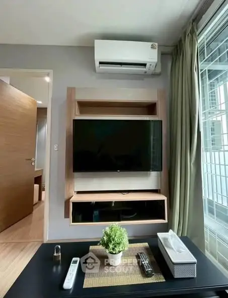 Modern living room with wall-mounted TV and air conditioning, featuring sleek wooden furniture and large window.